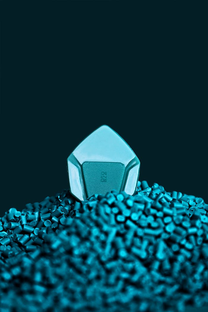 Close-up of a blue guitar pick resting atop a pile of plastic beads, studio shot.