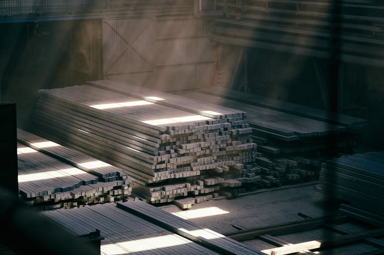 Sunlight streaming through an industrial warehouse highlighting stacked metal beams.